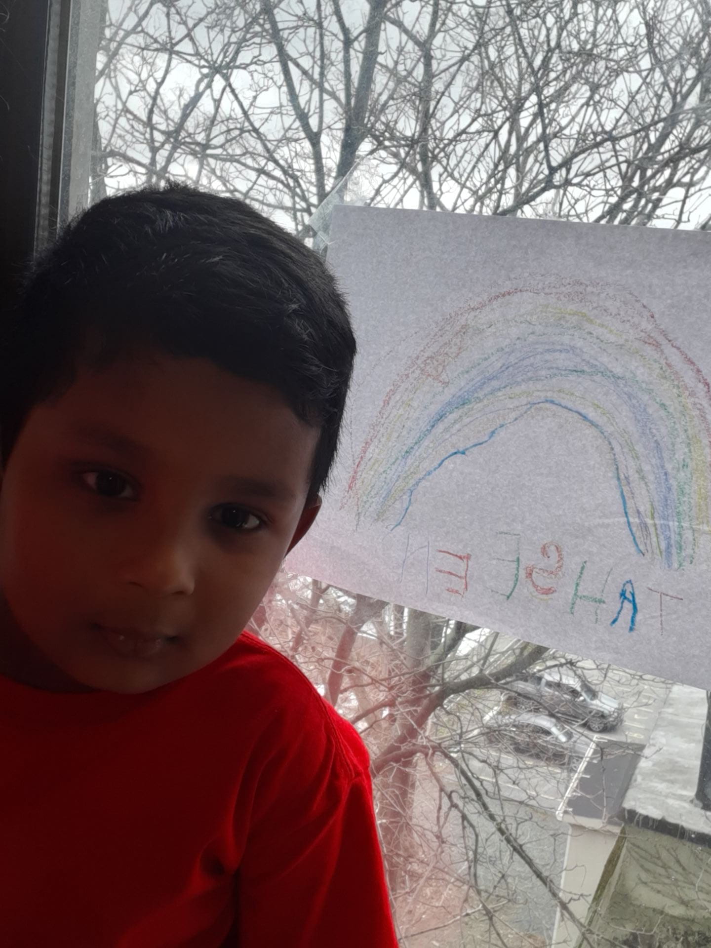 child standing by a window with a rainbow on it