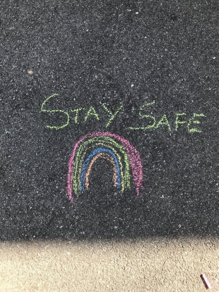 child drew a rainbow on the ground and wrote "stay safe"